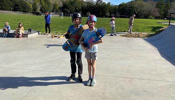 Two female students smiling and holding their skateboards at Valley Skate Park