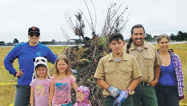 Parks staff and volunteers standing in front of a pile of pulled weeds